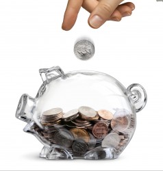 Concept of a businessman dropping a coin into a clear piggy bank half filled with coins isolated over white
