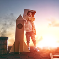 kid with a cardboard helmet and rocket looking at the horizon
