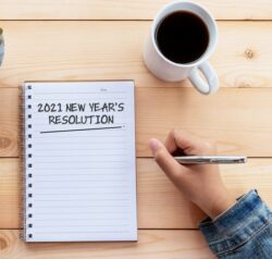 Hands Writing 2021 New Year's Resolution Text on Note Pad on Wood Desk