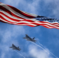 American flag blowing in wind and Lockheed Martin F-22 Raptors flying against sky